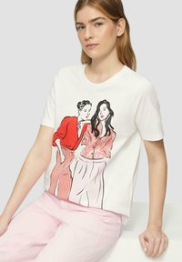 T-shirt blanc avec un motif imprimé de deux femmes en tenues rouges et roses. Tissu doux avec un col rond et des manches courtes.