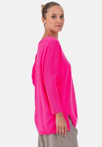 Pull rose vif oversize avec manches côtelées et fentes latérales. Texture douce et coupe décontractée, avec un col rond.