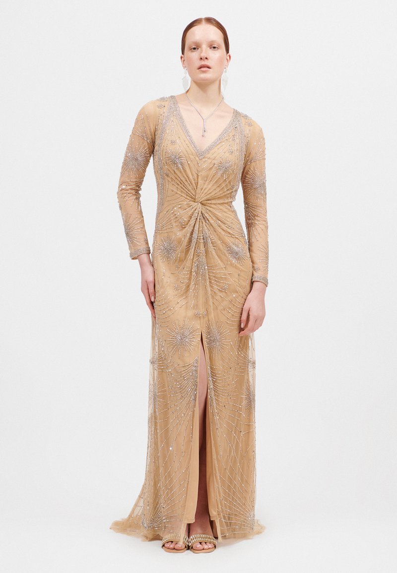 Beige avondjurk met kralen, lange mouwen, V-hals en een split. Heeft ingewikkeld zilveren kralenwerk en een aansluitende silhouette.