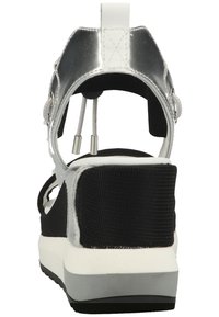 Black textile sandal with a silver rear strap, white sole, and adjustable hardware featuring a textured surface. Back view highlights design.