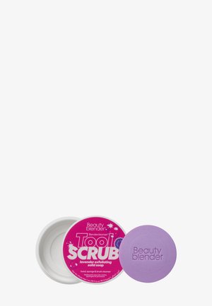 Savon solide lavande étiqueté "Nettoyant pour Outils de Maquillage Beauty Blender" avec un contenant ouvert blanc et une barre de savon violette gaufrée avec "Beauty blender."