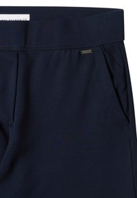 Marineblauwe broek met een elastische tailleband, voorzien van zijzakken en een klein metalen logoaccent nabij de tailleband. Gladde textuur.