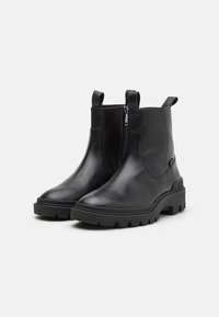 Mustad mustad nahast ankle saapad, millel on sile tekstuur, külgmine tõmblukk ja tugeva mustriga tald tractioni tagamiseks. Omab tõmblukke mugavaks selga panemiseks.