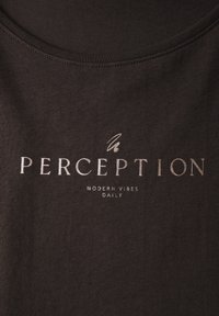 Černé látkové tričko se slovy "PERCEPTION" v metalicky stříbrné barvě, pod tím menším písmem "MODERN VIBES DAILY".