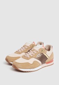 Un paio di sneakers in suede beige e marrone con lacci rosa chiaro e suole bianche, posate affiancate su uno sfondo semplice.