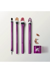 Cinq pinceaux de maquillage Real Techniques violets avec différentes nuances de poudre et de pigment, ainsi qu'un taille-crayon violet avec des copeaux de bois.