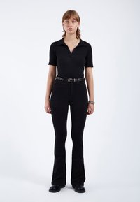 Camisa polo negra de canalé con mangas cortas, combinada con unos vaqueros negros de tiro alto y acampanados, acompañada de un cinturón de tejido y botas.