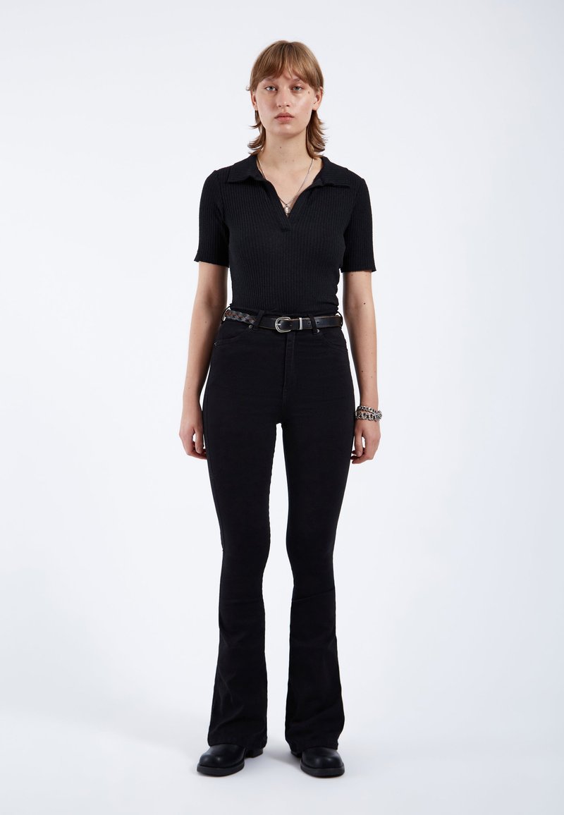 Camisa polo negra de canalé con mangas cortas, combinada con unos vaqueros negros de tiro alto y acampanados, acompañada de un cinturón de tejido y botas.