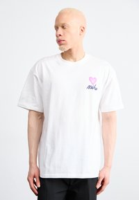 Camiseta de algodón blanca con mangas cortas. El gráfico en el pecho izquierdo incluye un corazón rosa y el texto en cursiva "Mike" en azul. Diseño sencillo.