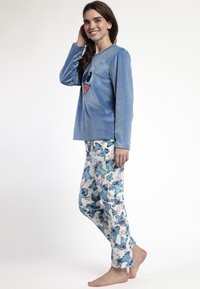 Top de pijama de peluche azul claro con escote redondeado y gráfico de personaje. Los pantalones blancos a juego presentan coloridos patrones de Stitch. Textura suave.