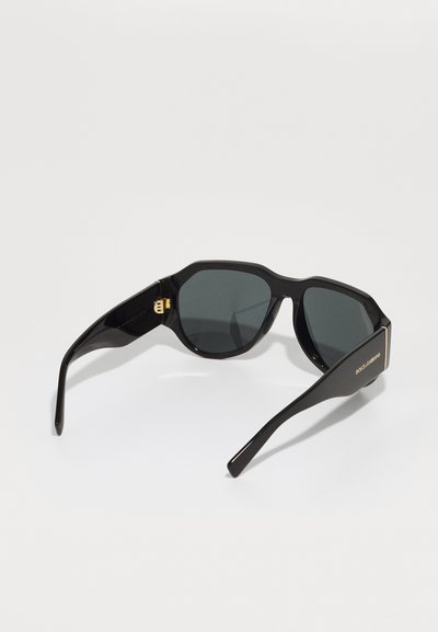Black sunglasses with an angular frame, dark lenses, and gold accents on the temples. Smooth plastic material with a shiny finish.