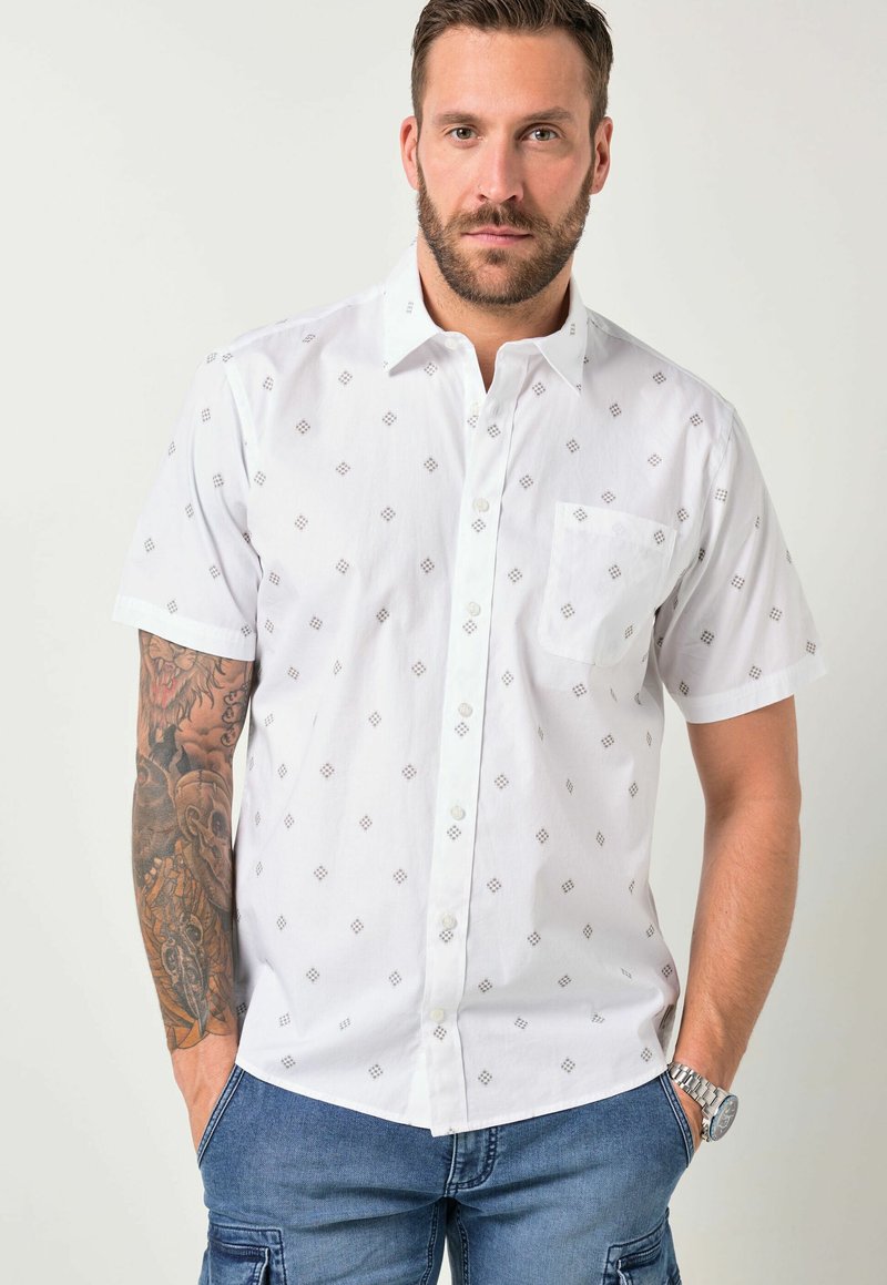 Man wearing a white short-sleeve button-up shirt with a small diamond pattern and blue cargo pants with hands in pockets.