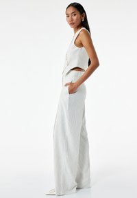 Tweeded outfit in het wit met verticale strepen. Mouwloze top met een lichte crop en knoopdetails; wijde broek met zakken.