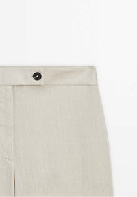Ceinture de pantalon en lin beige avec un bouton noir et des détails de couture visibles sur fond blanc.
