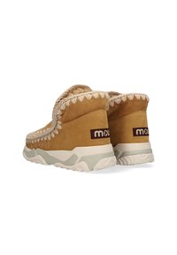 Bruine suède enkellaarsjes met beige bontvoering en decoratieve stiksel; voorzien van een wit en lichtgrijze zool. Merken zijn zichtbaar aan de zijkant.