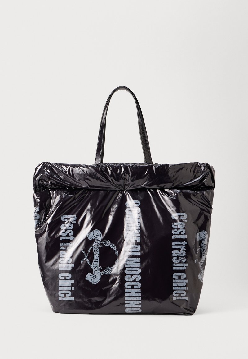 Black tote bag made of shiny material with a reversible design. Features long black handles and printed text in light blue.