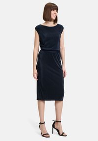 Navyblaues Kleid aus geripptem Stoff, mit Bootsausschnitt, kurzen Ärmeln und tailliertem Schnitt. Kombiniert mit schwarzen, verzierten Absätzen.