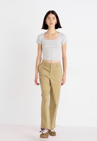 Cropped top grigio a maniche corte abbinato a pantaloni dritti color khaki e scarpe con stampa animale. La modella è in piedi con le mani sui fianchi, su uno sfondo neutro.