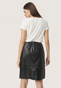 Bílý top s krátkým rukávem v kombinaci s těsně padnoucími černými koženými sukněmi. Sukně má zip na zadní straně a hladkou texturu.