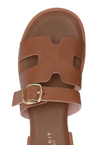 Bruin leren sandaal met uitgesneden ontwerp, verstelbare enkelband met gouden gesp en platte zool, met een gladde textuur.
