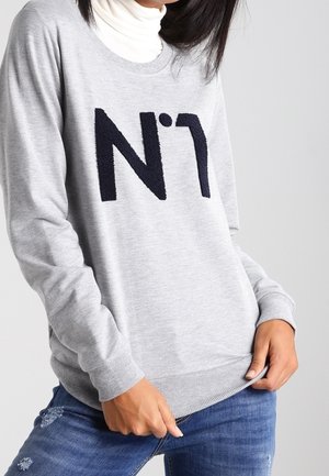 Felpa grigia con il ricamo blu navy "N°1" sul davanti, colletto a giro, polsini e orlo a costine. Abbinata a jeans blu strappati.