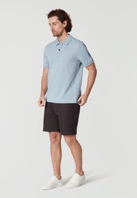 Světle modré polo tričko s krátkými rukávy, s knoflíkovým límcem. V kombinaci s černými šortkami a bílými teniskami. Jednoduchý a čistý design.