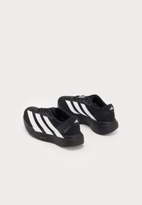 Mustad mustad Adidas jooksujalatsid mustade valgete triipudega, paksu pehme tallaga ja paeltega, nähtud tagant kolmanda nurga alt valgel taustal.
