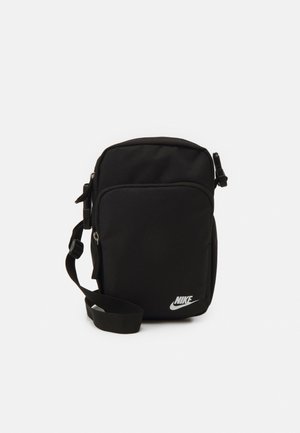 Black nylon crossbody bag with adjustable strap, zippered compartments, and a white Nike logo on the front. Smooth texture, rectangular shape.