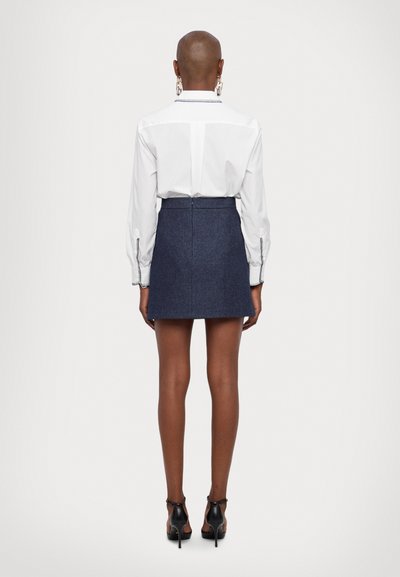 White long-sleeve shirt with button details, paired with a dark blue denim mini skirt. Accessories include large hoop earrings and black heels.