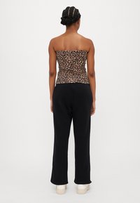 Calças de moletom pretas combinadas com um top sem alças de padrão de leopardo. O top tem um design justo, enquanto as calças são largas e casuais.