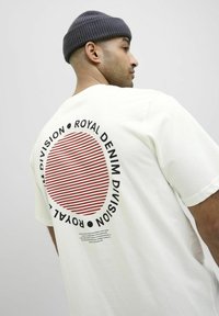 Hvid oversized T-shirt med et stort rødt og hvidt stribet cirkeldiagram på ryggen, omkranset af sort tekst. Blødt stof, afslappet pasform.