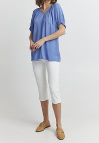 Jasnoniebieski top z krótkim rękawem z marszczonymi ramionami, zestawiony z białymi spodniami 7/8 i brązowymi mokasynami, eksponując gładkie tekstury.