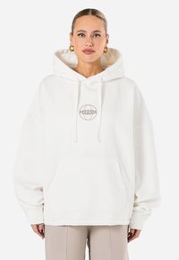 Biela oversize mikina z mäkkého materiálu s predným vreckom a vyšívaným kruhovým logom "PEGADOR" v sivej farbe.