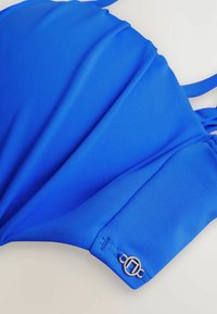 Königsblaues Bikini-Oberteil mit einer glatten, strukturierten Oberfläche. Verfügt über verstellbare Träger und ein Metall-Logo-Detail in der Nähe des Verschlusses.
