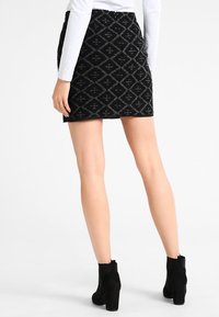 Černá mini sukně s geometrickým vzorem, strukturovanou tkaninou a přiléhavým střihem. Noste s černými kotníkovými botami.