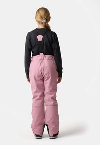 Lyserøde snebukser med sorte justerbare stropper, en glat tekstur og elastiske manchetter. Reflekterende detaljer ved benene øger synligheden.