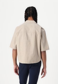 Chemise à manches courtes, beige, à boutons, avec des rayures verticales bleu marine, dotée d'un empiècement au dos et d'une coupe décontractée.