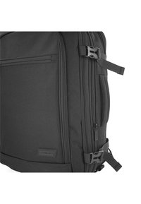 Mochila negra con una textura suave y mate; cuenta con múltiples compartimentos con cremallera, correas ajustables y una etiqueta de marca.