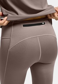 Tights i en dämpad mauve-färg, tillverkade av ett slätt, elastiskt tyg. Har en säker svart dragkedjeficka bak. Sömmen är förstärkt.