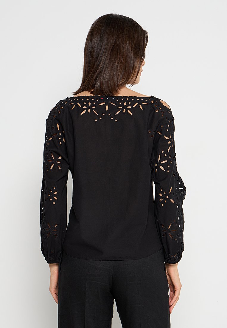 Czarna bluzka z długimi rękawami, zdobiona skomplikowanymi wycięciami w kwiatowe wzory wzdłuż ramion i rękawów. Gładki, lekki materiał.