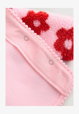 Pink fleece tæppe med en tekstureret overflade, der prydes af røde blomsterdesigns, kantet med pom-pom detaljer og trykknapper i kanten.