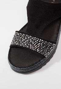Sandale compensée noire avec semelle texturée, dotée d'une tige en daim et d'une bride avant ornée de petits strass réfléchissants.