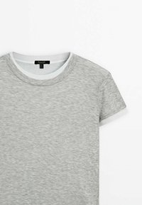 T-shirt gris clair à manches courtes avec col rond, bordé de blanc au niveau du col et des manches, posé à plat sur un fond blanc.