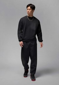Zwarte sweatshirt met een textuur op de schouders, gecombineerd met zwarte sweatpants met gaasaccenten en zwarte sneakers met rode details.