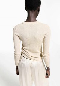 Maglietta a maniche lunghe in maglia a costine di un beige metallico; design aderente con scollatura tonda, abbinata a pantaloni leggeri e fluttuanti di colore chiaro.