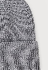 Gray knitted beanie with a ribbed texture, featuring a rolled cuff. The yarn is thick and soft, providing warmth and comfort.