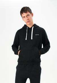 Black hoodie made of soft fabric featuring a front kangaroo pocket, white drawstrings, and a small logo on the chest.