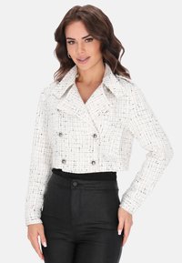 Lyhennetty valkoinen tweed-takki, jossa on ruutukuosi, kaksirivinen etuosa, suuri kaulus ja hopeiset nappikoristeet. Yhdistetty mustiin pantsuihin.