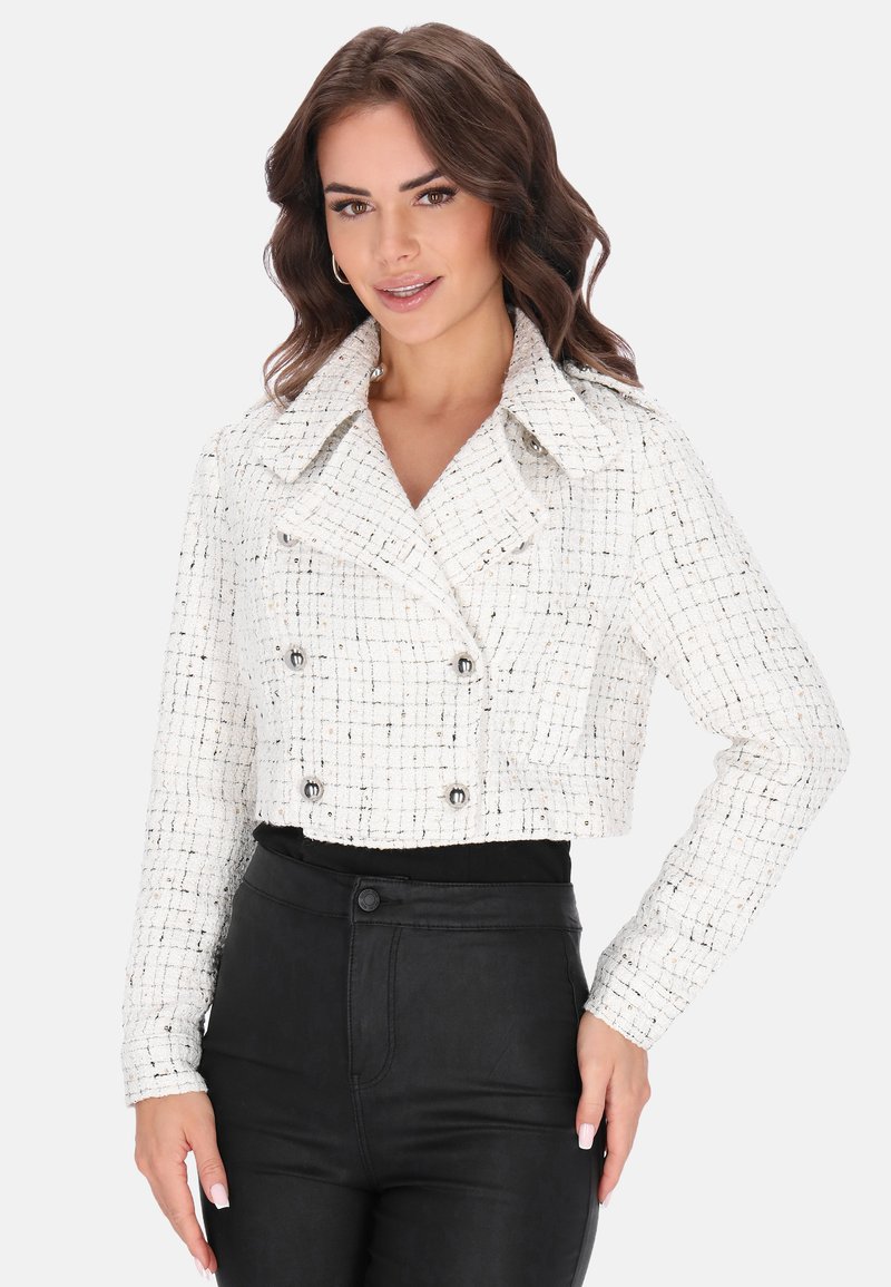 Lyhennetty valkoinen tweed-takki, jossa on ruutukuosi, kaksirivinen etuosa, suuri kaulus ja hopeiset nappikoristeet. Yhdistetty mustiin pantsuihin.