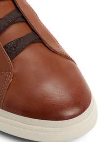 Nahaufnahme einer braunen Ledersneaker-Spitze mit dunklen elastischen Seitenriemen und weißer Gummisohle.